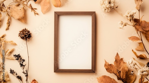 Rustic autumn backdrop with an empty photo frame, dried flowers, and a branch on a warm beige surface. Arranged flat for a top view with copy space for a mockup.