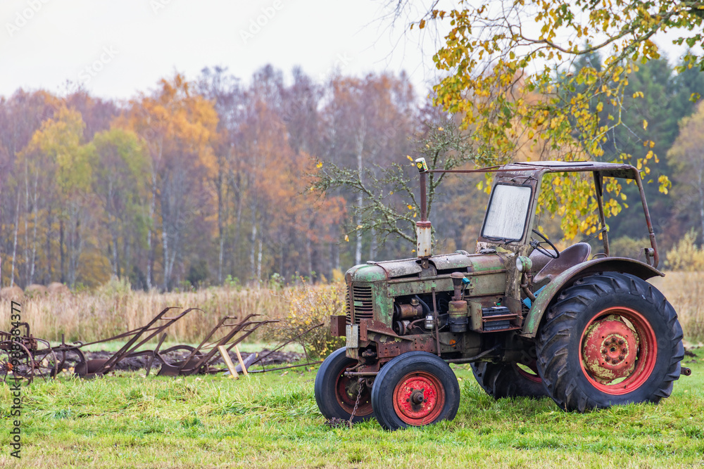 Obraz premium Old tractor with old agricultural tools on a meadow in an autumn landscape
