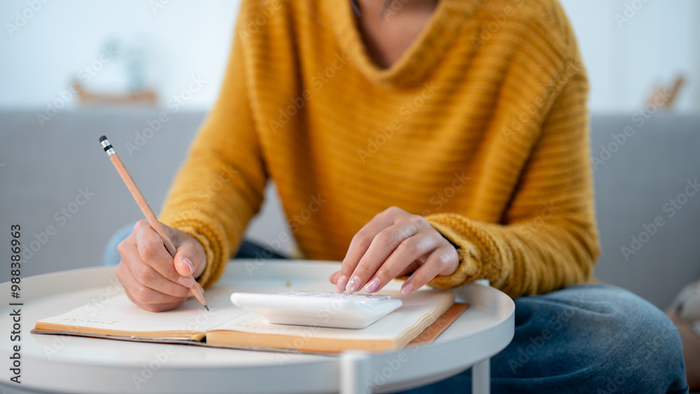 A woman writing in a book and using a calculator to manage her household expenses. A woman writing in a book and using a calculator to manage her household expenses.