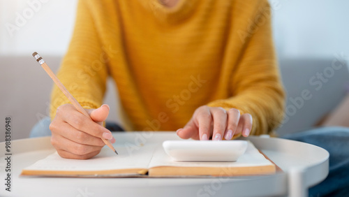 A woman writing in a book and using a calculator to manage her household expenses.