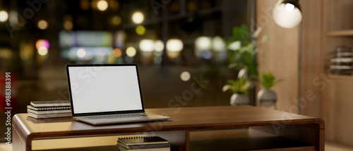 A laptop sits on a hardwood coffee table by a window with a night city view in a cozy living room.