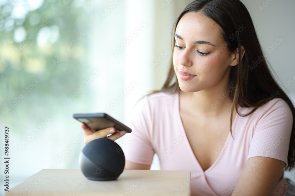 Serious woman pairing smart speaker with phone Serious woman pairing smart speaker with phone