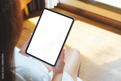 Mockup image of a woman holding digital tablet with blank desktop screen on the bed