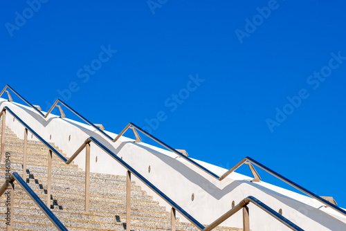 A modern outdoor staircase with sleek railings ascending under a vibrant blue sky demonstrating architectural beauty and clear weather conditions. photo