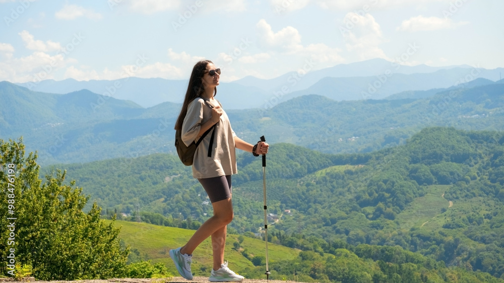 Naklejka premium Woman stands on observation deck with walking sticks and contemplating the mountains.