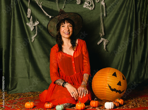 Portrait of a cute young woman in a red dress and a witch hat at a Halloween party photo