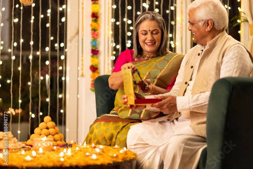 Happy senior husband giving surprise gift to excited wife in illuminated home on occasion of Diwali festival photo