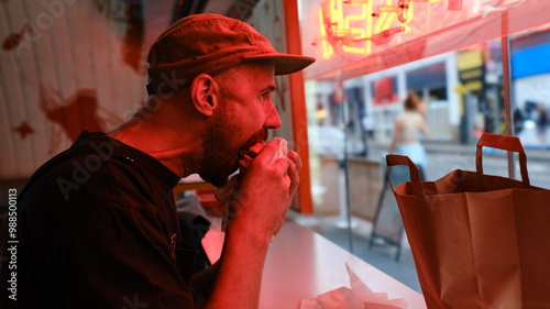 Man eating sandwich near red neon lighting at fast food restaurant
