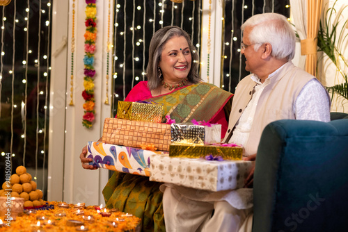 Happy senior husband giving surprise gift to excited wife in illuminated home on occasion of Diwali festival photo