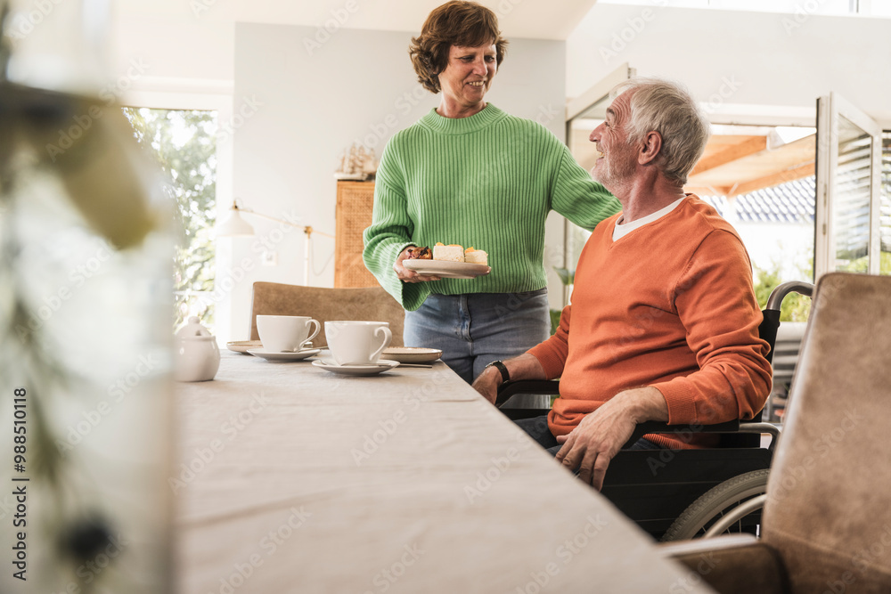 Smiling woman serving sliced cake to husband on wheelchair at home Smiling woman serving sliced cake to husband on wheelchair at home
