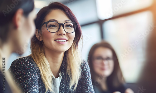 A smiling woman in glasses, listening to a conversation, looking interested in a meeting or discussion.