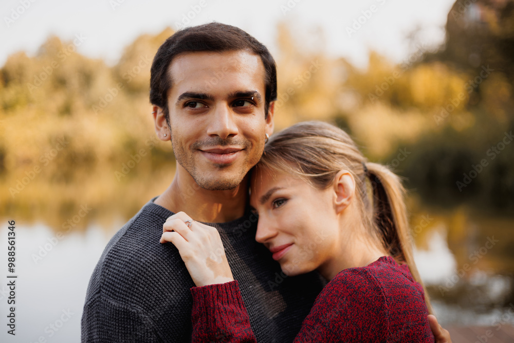 Fototapeta premium Young romantic couple looking away near blurred lake in autumn