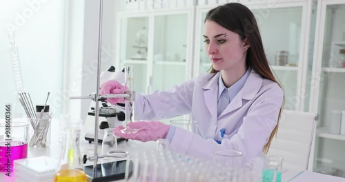 Woman scientist carefully places beaker under burette in laboratory. Female worker in uniform prepares equipment for scientific experiment