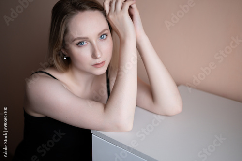 Graceful young woman in a black top posing against beige wall.