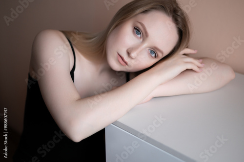Graceful young woman in a black top posing against beige wall.