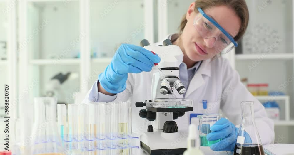 Woman chemist places sample under microscope with pipette in laboratory. Professional technician conducts scientific research and analysis Woman chemist places sample under microscope with pipette in laboratory. Professional technician conducts scientific research and analysis