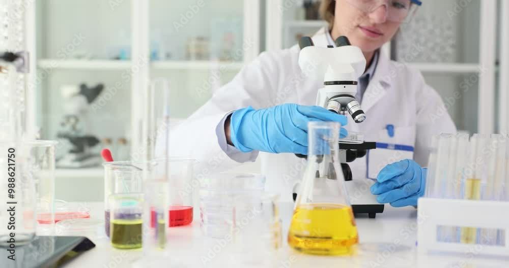 Woman assistant places glass slide with sample on microscope in medical lab. Biologist researches substance specimen with lab tools near glassware Woman assistant places glass slide with sample on microscope in medical lab. Biologist researches substance specimen with lab tools near glassware