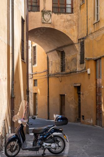 Iconic Italian lifestyle scene with scooter moped transport parked in overhead arched stone walled alleyway in streets of Pisa, Tuscany, Italy. 