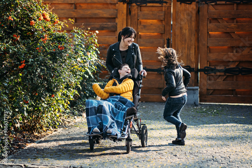 Εκτύπωση καμβά Mother and sibling bonding with child in wheelchair during outdoor time, special needs care, family strength, nature connection, disability inclusion