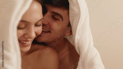 A beautiful couple sharing a romantic moment, flirting and kissing under a cozy blanket in bed, radiating happiness and love.