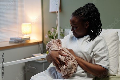 Obraz na plátně Black woman sitting in hospital bed in softly lit room, tenderly cradling her ne