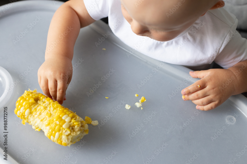 Obraz premium Little child picking by fingers sweet corn kernels from the table. Closeup.