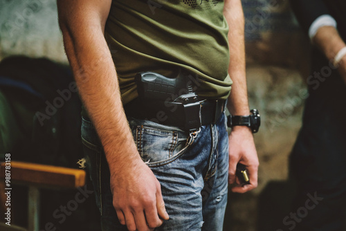 Armed man in jeans and green shirt with holstered handgun and wristwatch, standing. Gun magazine. Handgun photo