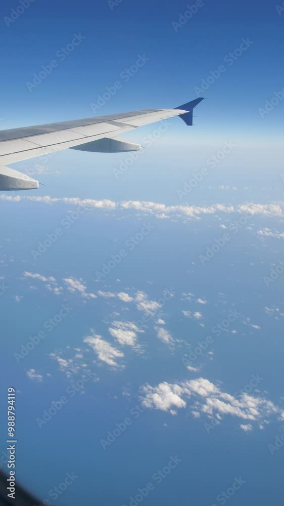 vertical screen: a view out the window of an airplane flying over the ocean. View from the airplane window of clouds and the blue expanse of the sea or ocean. Skyscape from inside a passenger airliner vertical screen: a view out the window of an airplane flying over the ocean. View from the airplane window of clouds and the blue expanse of the sea or ocean. Skyscape from inside a passenger airliner
