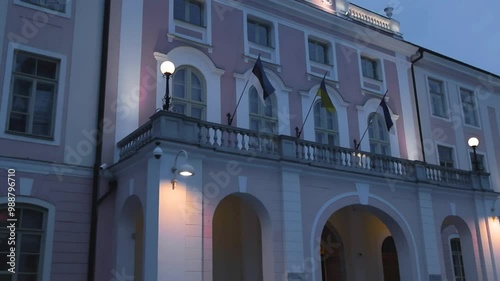 Slow motion footage of Estonian parliament building with Estonian and Ukraine flags waving the wall. The pink building is lit cinematically and filmed during night evening or dusk with cloudy weather. photo