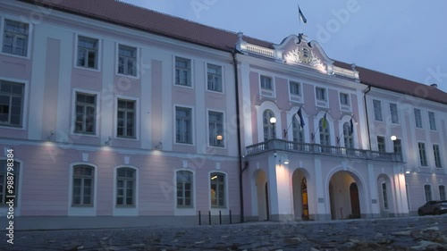 Footage shows Estonian government parliament building during an autumn evening or night while the building is lit with lights. An Estonian flag is waving in slow motion on the top and clouds visible. photo