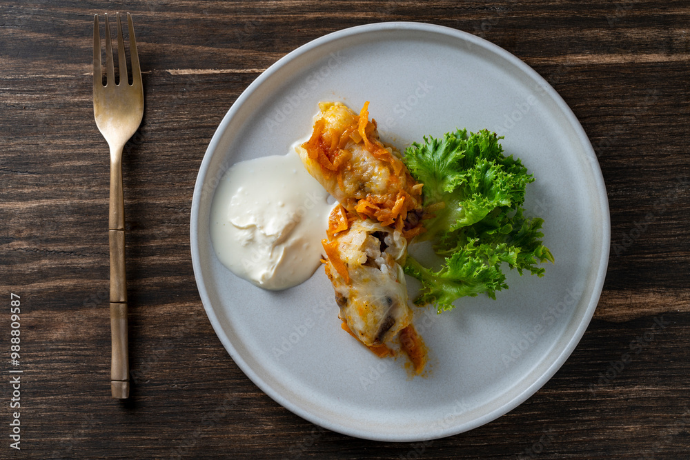 Two delicious cabbage rolls stuffed with meat and rice on a plate along with sour cream and lettuce, closeup, top view Two delicious cabbage rolls stuffed with meat and rice on a plate along with sour cream and lettuce, closeup, top view