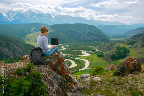 Woman works remotely on a mountain ridge in summer beautiful day.
