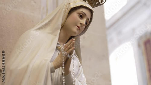 serene statue of the Virgin Mary, hands clasped in prayer, adorned with a crown and holding rosary beads, symbolizing devotion and faith photo