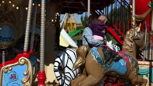 Wallpaper Mural A mother smiles at her baby daughter while riding a horse on a vintage carousel at an amusement park. The carousel horses are brown, white, and blue.  Torontodigital.ca