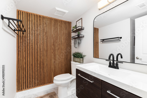 A bathroom with a dark wood cabinet, floating shelves with decorations above the toilet, and a wood slat accent wall.