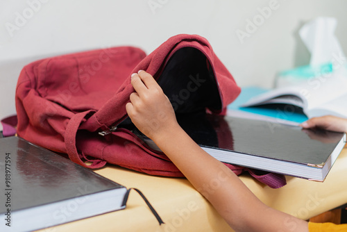 Child Packing School Books Into a Red Backpack at Home