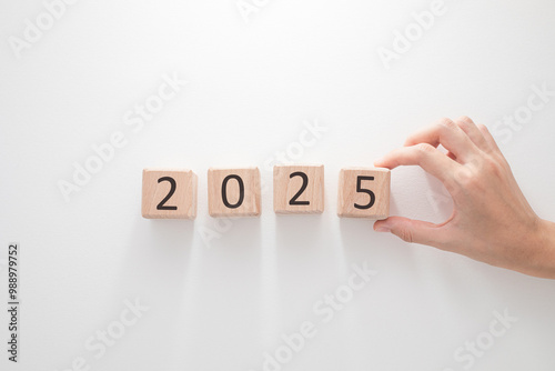 A hand arranging wooden blocks to display the year 2025 on a clean white background.