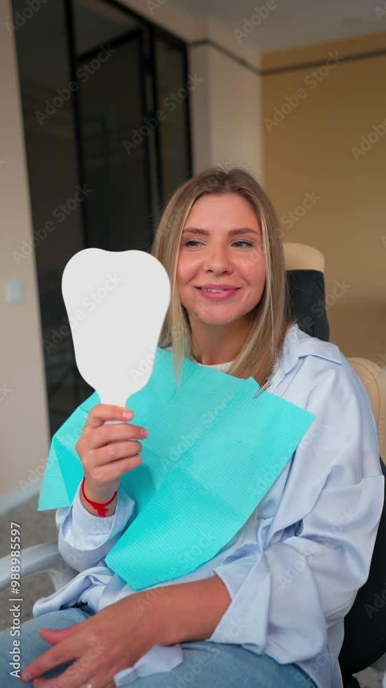 Female Patient Looks at Her Healthy Smile in Mirror after Dental Treatment in a Dental Clinic. Concept of Modern Medicine and Health. Vertical Video. Slow Motion. Female Patient Looks at Her Healthy Smile in Mirror after Dental Treatment in a Dental Clinic. Concept of Modern Medicine and Health. Vertical Video. Slow Motion.