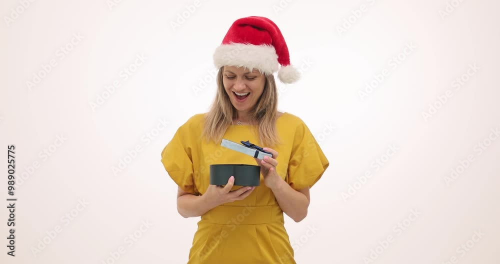 Joyful woman in Santa hat opens Christmas gift from beloved partner on white background. Surprise blonde lady in yellow receives holiday present Joyful woman in Santa hat opens Christmas gift from beloved partner on white background. Surprise blonde lady in yellow receives holiday present