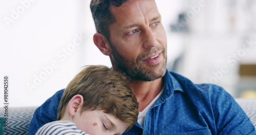 A happy, loving and caring father holding his son as he sleeps in his arms or lap while sitting on a sofa. Young family man relaxing on a couch after spending the day bonding together with his child photo