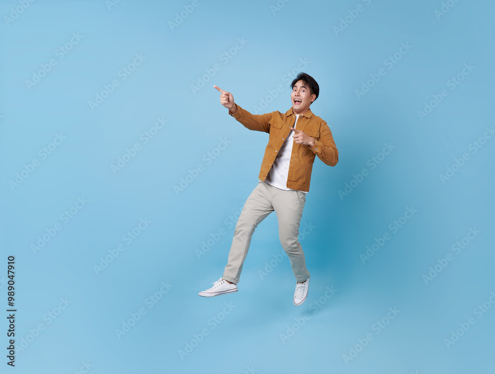 Full length Asian man jumping with hand pointing finger isolated on blue copy space background. Full length Asian man jumping with hand pointing finger isolated on blue copy space background.