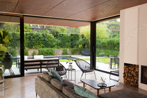 Modern living room with large windows overlooking backyard pool and garden, copy space