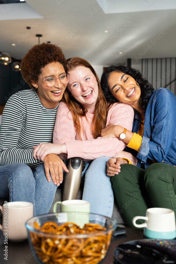 Friends hugging and laughing on couch, enjoying snacks and coffee together Friends hugging and laughing on couch, enjoying snacks and coffee together