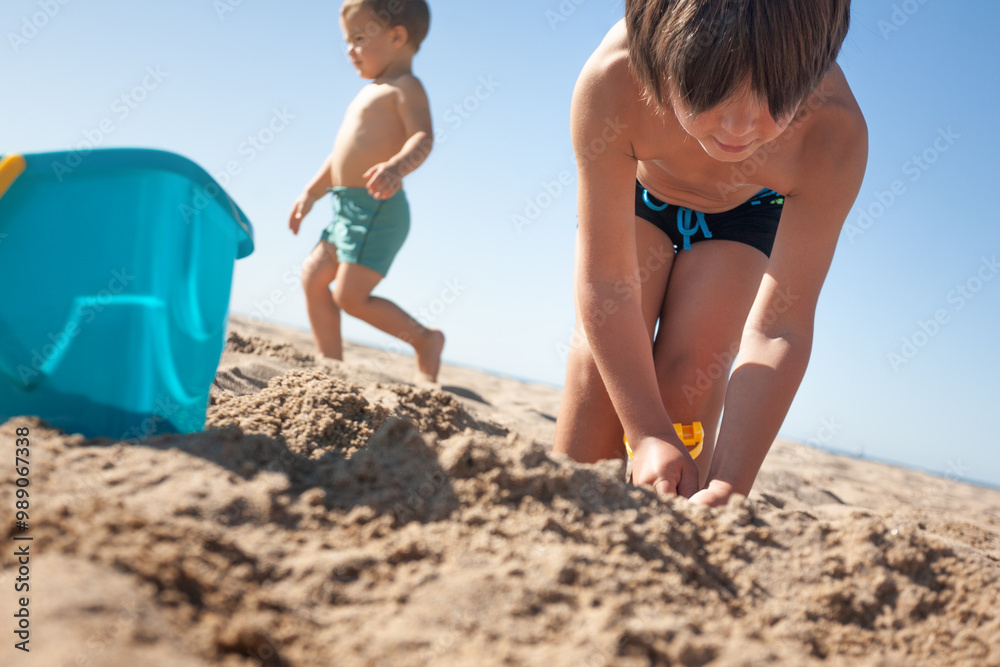 Children wearing swimsuits are digging in the sand of a beach.