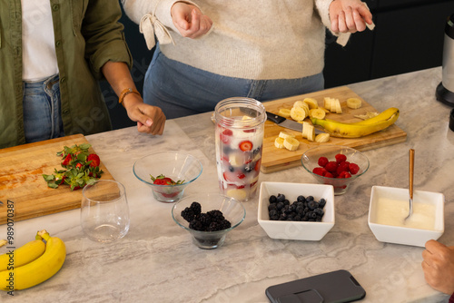 Chopping fruits and mixing ingredients, friends preparing fresh fruit smoothie together