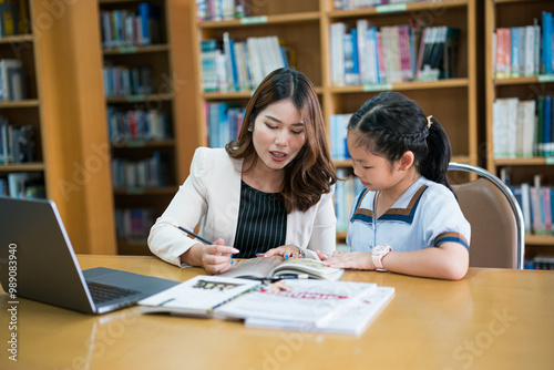 Teacher Helping Young Student with Schoolwork in Library. A teacher guides a young student with schoolwork in a library setting, focusing on personalized learning and academic development.