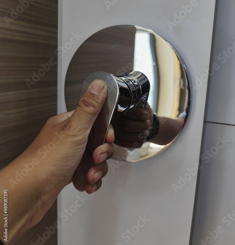 A hand turns a round, chrome-plated shower faucet. The faucet has a single lever handle and a circular base