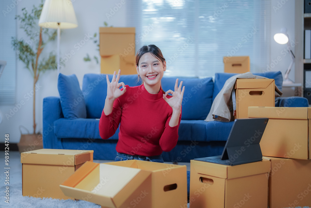 Smiling young woman is gesturing ok with both hands while unpacking cardboard boxes in her living room, concept of moving home Smiling young woman is gesturing ok with both hands while unpacking cardboard boxes in her living room, concept of moving home