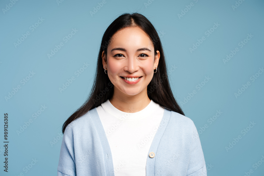 Smiling Asian woman wearing blue sweater looking at camera standing isolated on blue background Smiling Asian woman wearing blue sweater looking at camera standing isolated on blue background