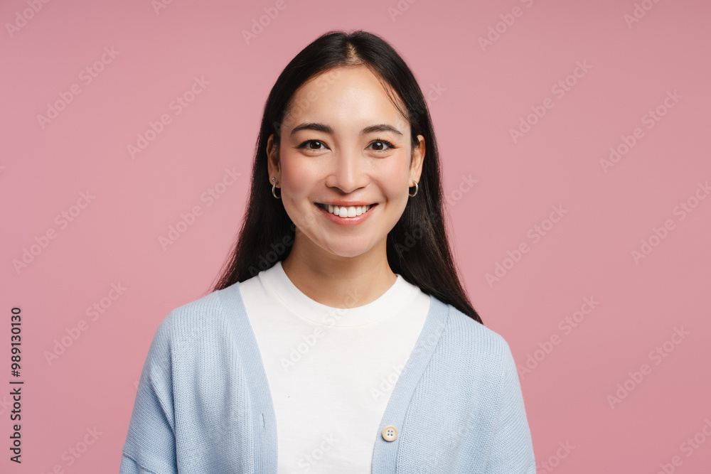 Young, smiling Asian woman smiling wearing blue cardigan posing isolated on pink background